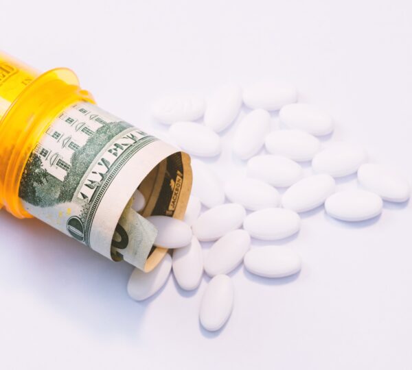 Pills coming out of a pill bottle with a twenty dollar bill inside, medical expense concept