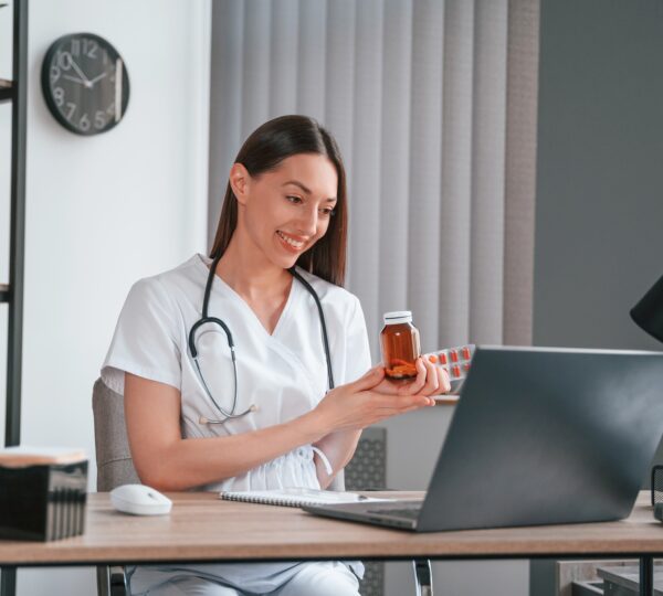 Speaking online. Pills is on the table. Young beautiful female doctor in white coat is in the office
